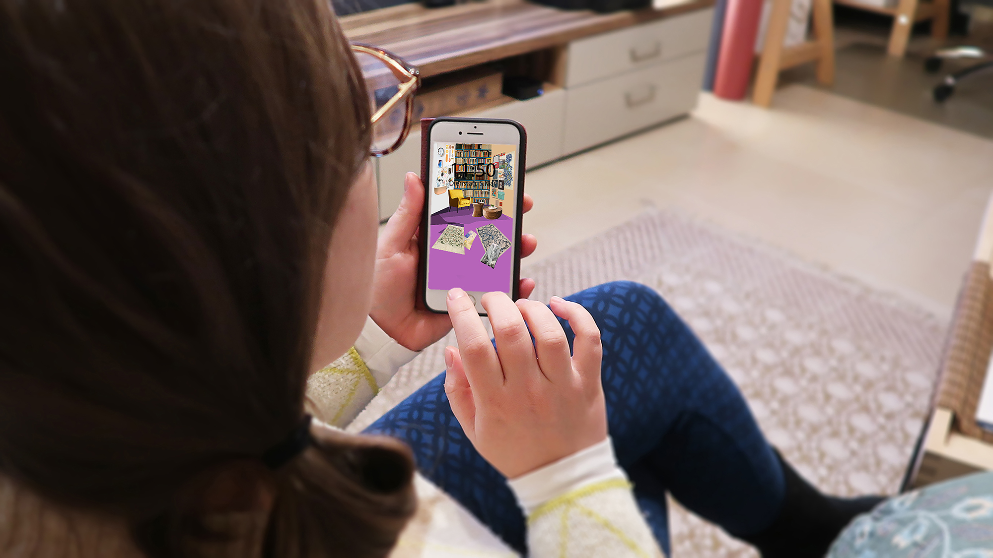 A person sitting in a room is holding a smartphone in their hand displaying a self-created collage of a room on its home screen.